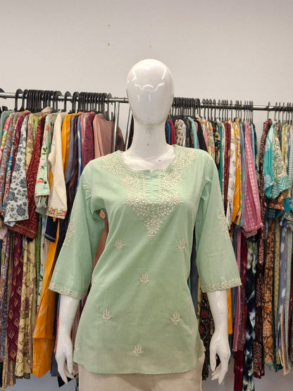 Light green embroidered top on a mannequin with a clothing rack in the background