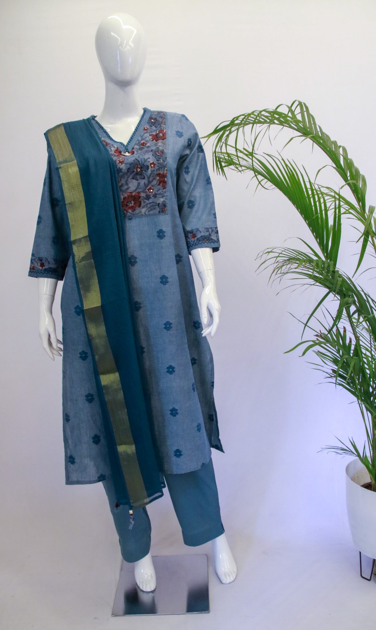 A blue Kota dupatta set displayed on a mannequin, consisting of a kurta with V-neck and sequence work, and matching pants with an elastic drawstring. The set is presented against a backdrop with a potted plant and a white background.