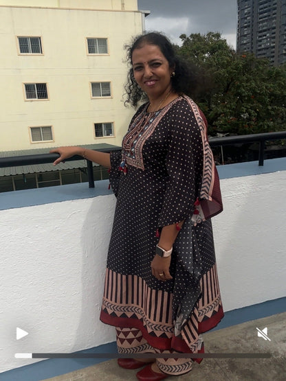 Woman in a patterned dress standing on a rooftop with buildings and trees in the background