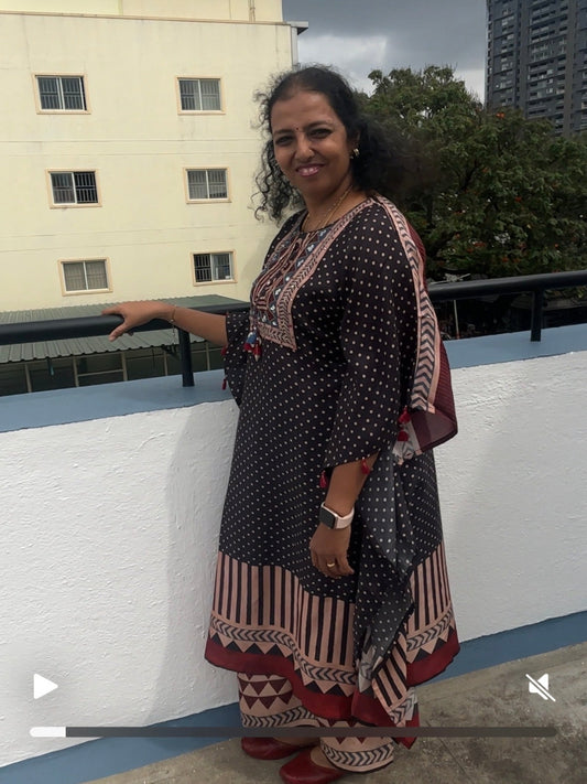 Woman in a patterned dress standing on a rooftop with buildings and trees in the background
