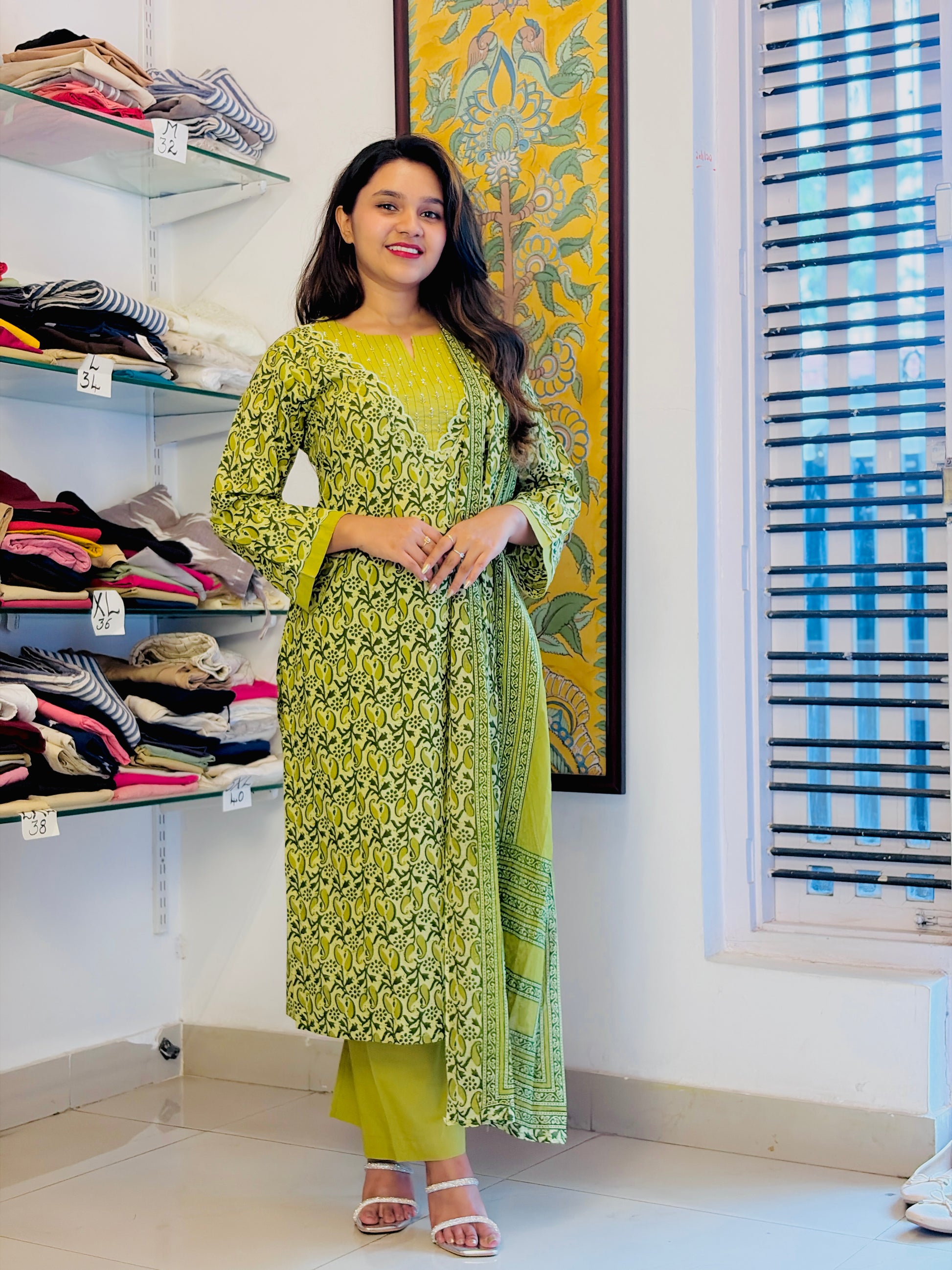A woman modeling a green printed kurta with matching pants and dupatta in a boutique setting.