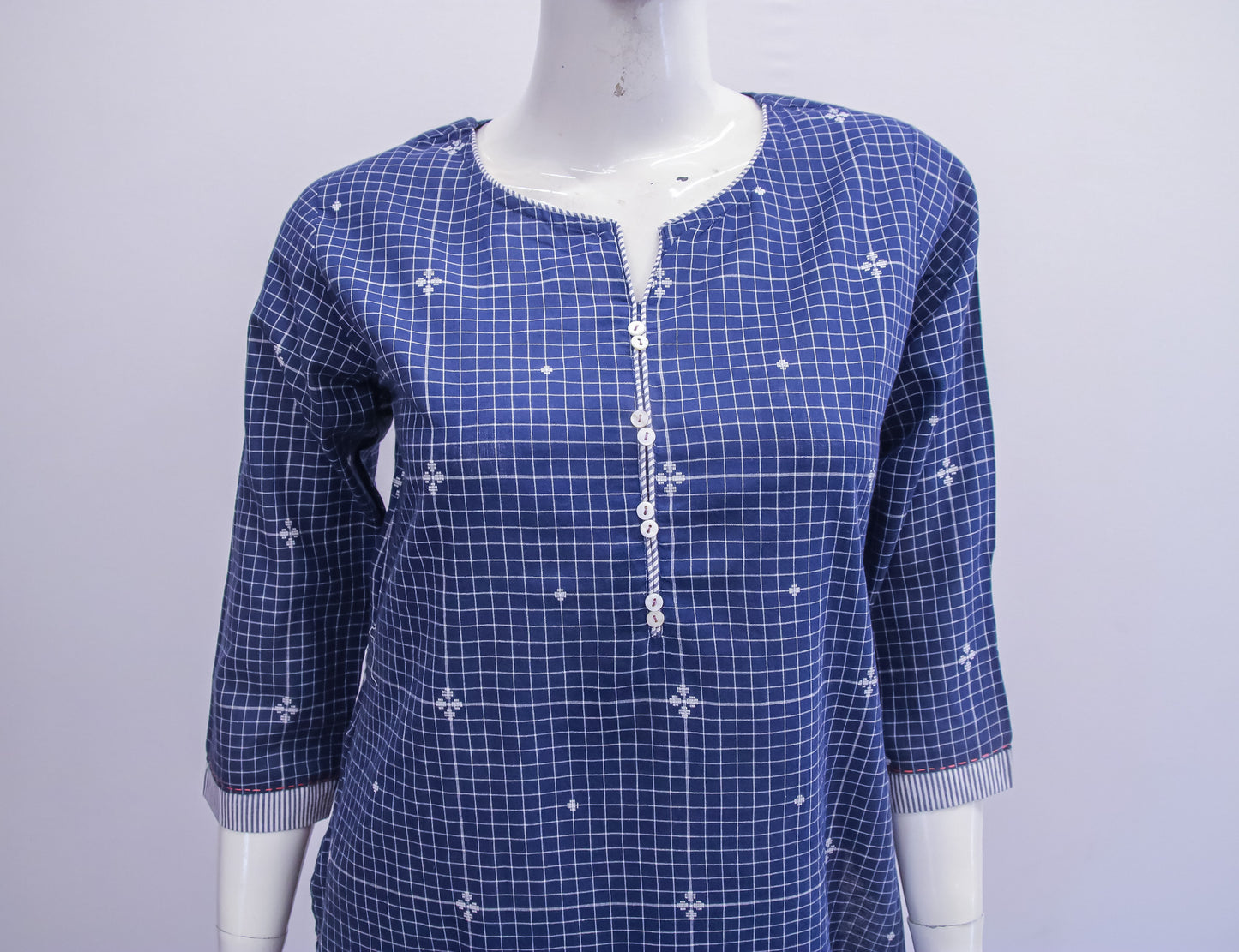 Blue checkered dress with white floral patterns on a mannequin against a light gray background