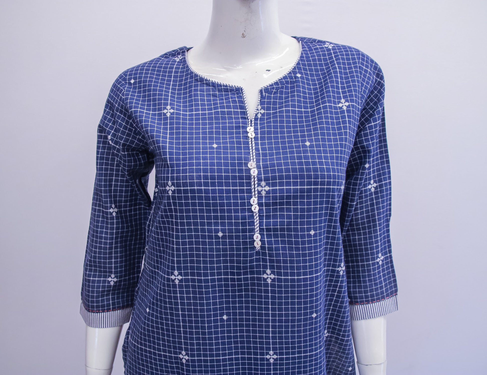 Blue checkered dress with white floral patterns on a mannequin against a light gray background