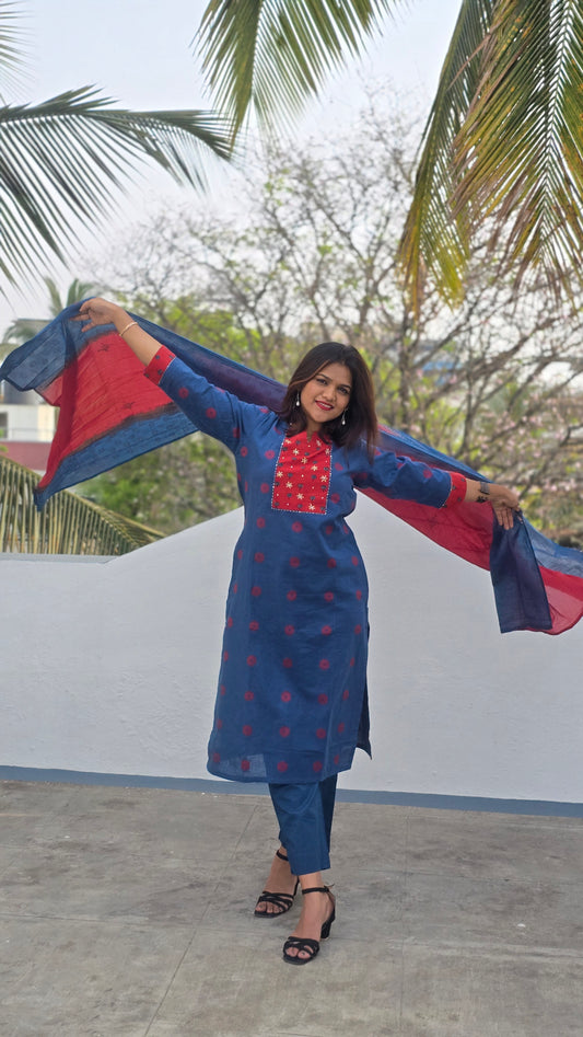 Woman in a blue and red outfit standing outdoors with palm trees in the background