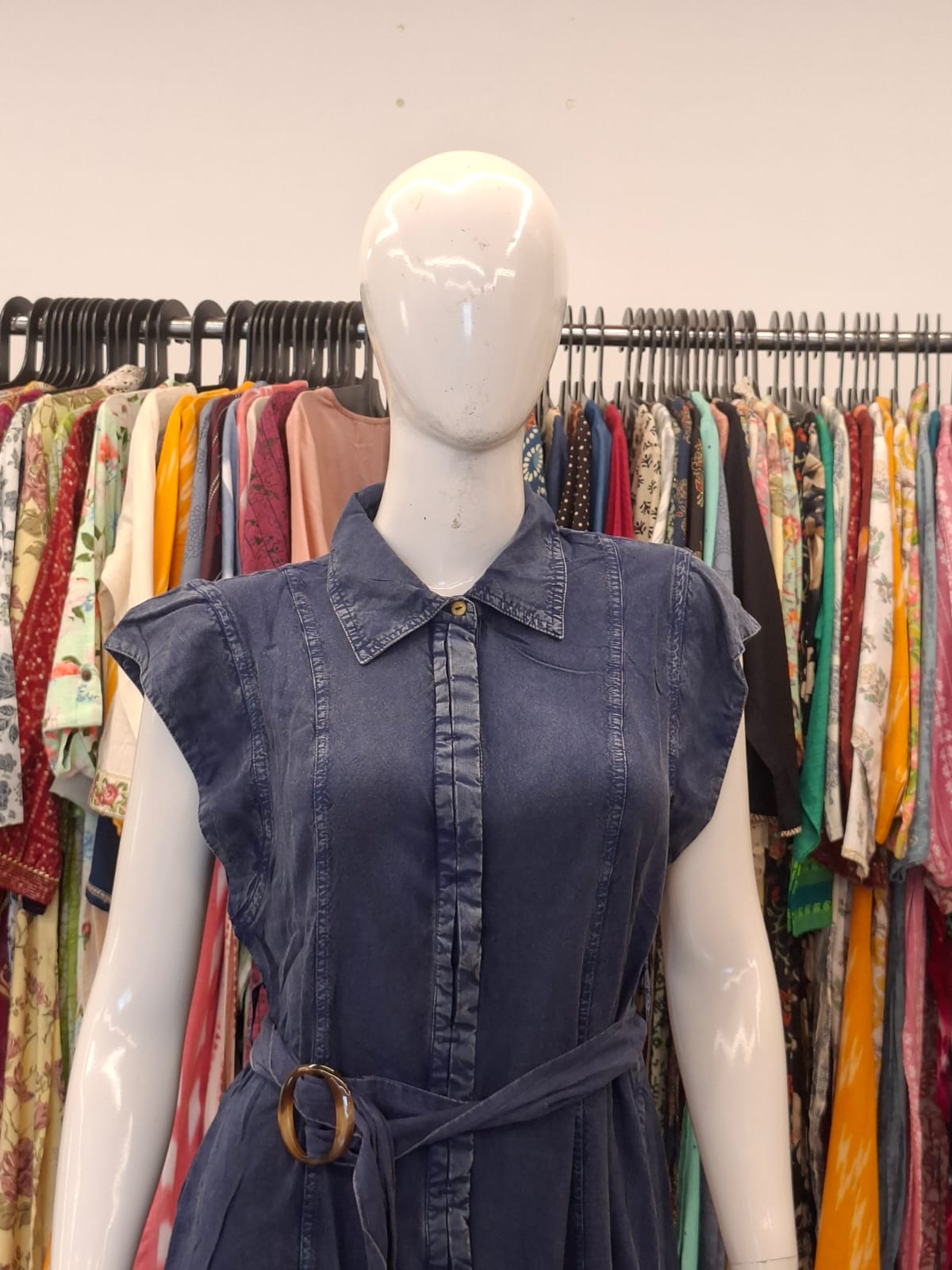 Mannequin wearing a blue denim dress with a colorful clothing rack in the background
