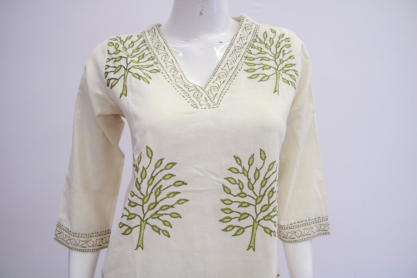 White top with green leaf patterns on a mannequin against a white background