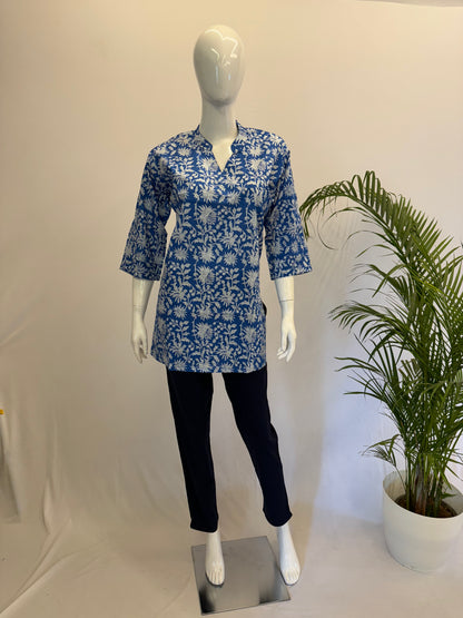 Mannequin wearing a blue floral patterned shirt and black pants with a plant in the background.