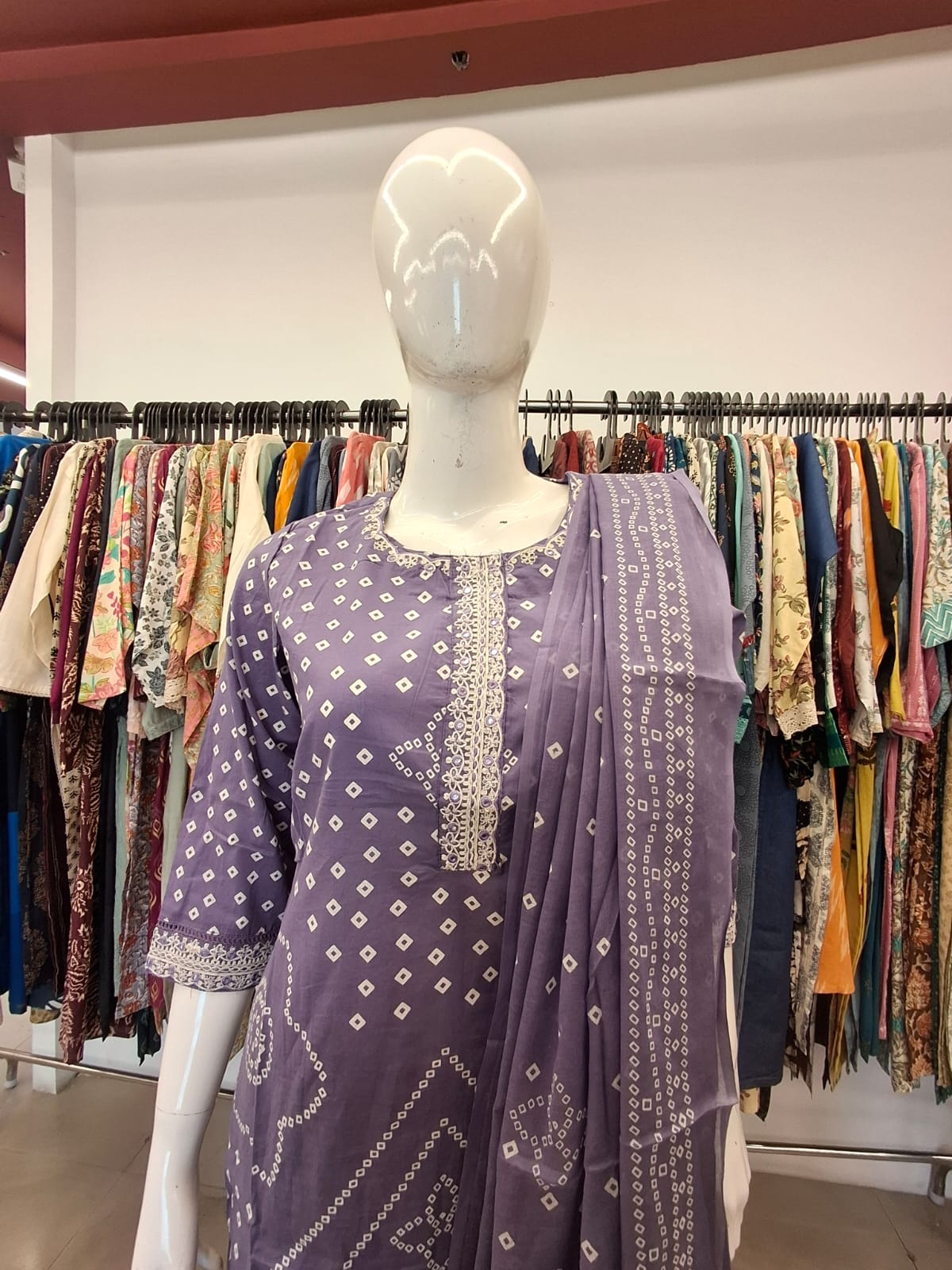 Mannequin wearing a purple patterned outfit with a background of clothing racks.