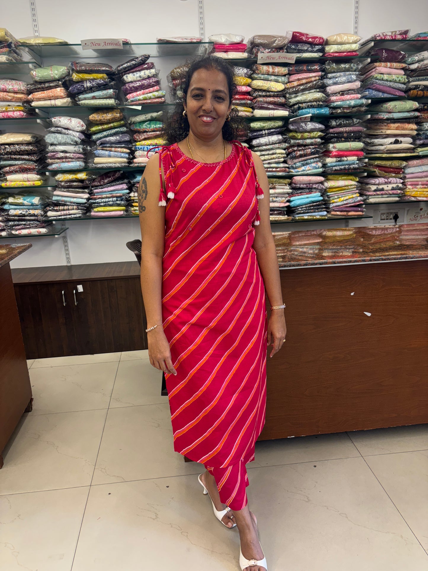Woman holding a red and orange striped saree in front of a wall of folded clothes.