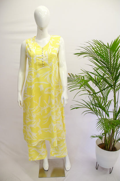 A mannequin displaying a light yellow top and pant set with a floral print, standing next to a potted plant.