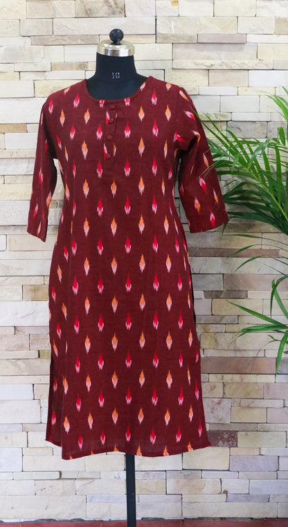 A red cotton kurta with ikkath print displayed on a mannequin against a brick wall backdrop.