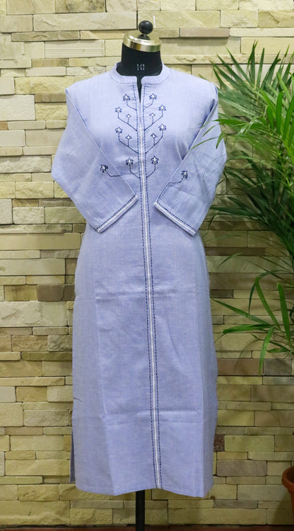 A light blue, premium cotton kurta with handwork on the yoke, displayed against a brick wall background.