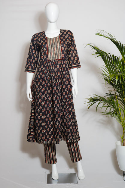 A dark brown cotton top and pant set with a floral print, displayed on a mannequin against a white background, with green leaves in the background.