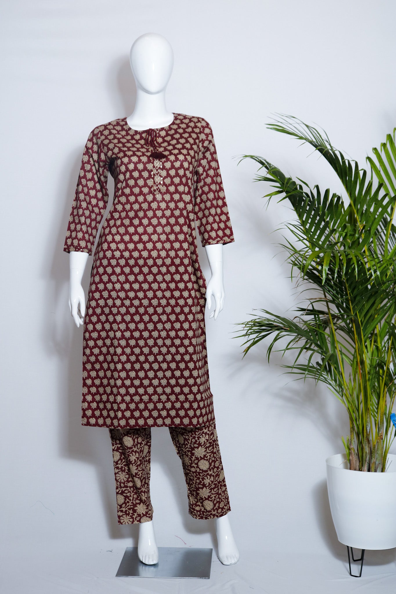 Maroon cotton top and pant set displayed on a mannequin with floral print on the pants, standing in a retail setting with a plant in the background.