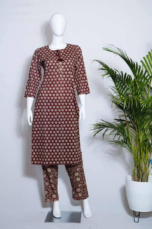 Maroon cotton top and pant set displayed on a mannequin with floral print on the pants, standing in a retail setting with a plant in the background.