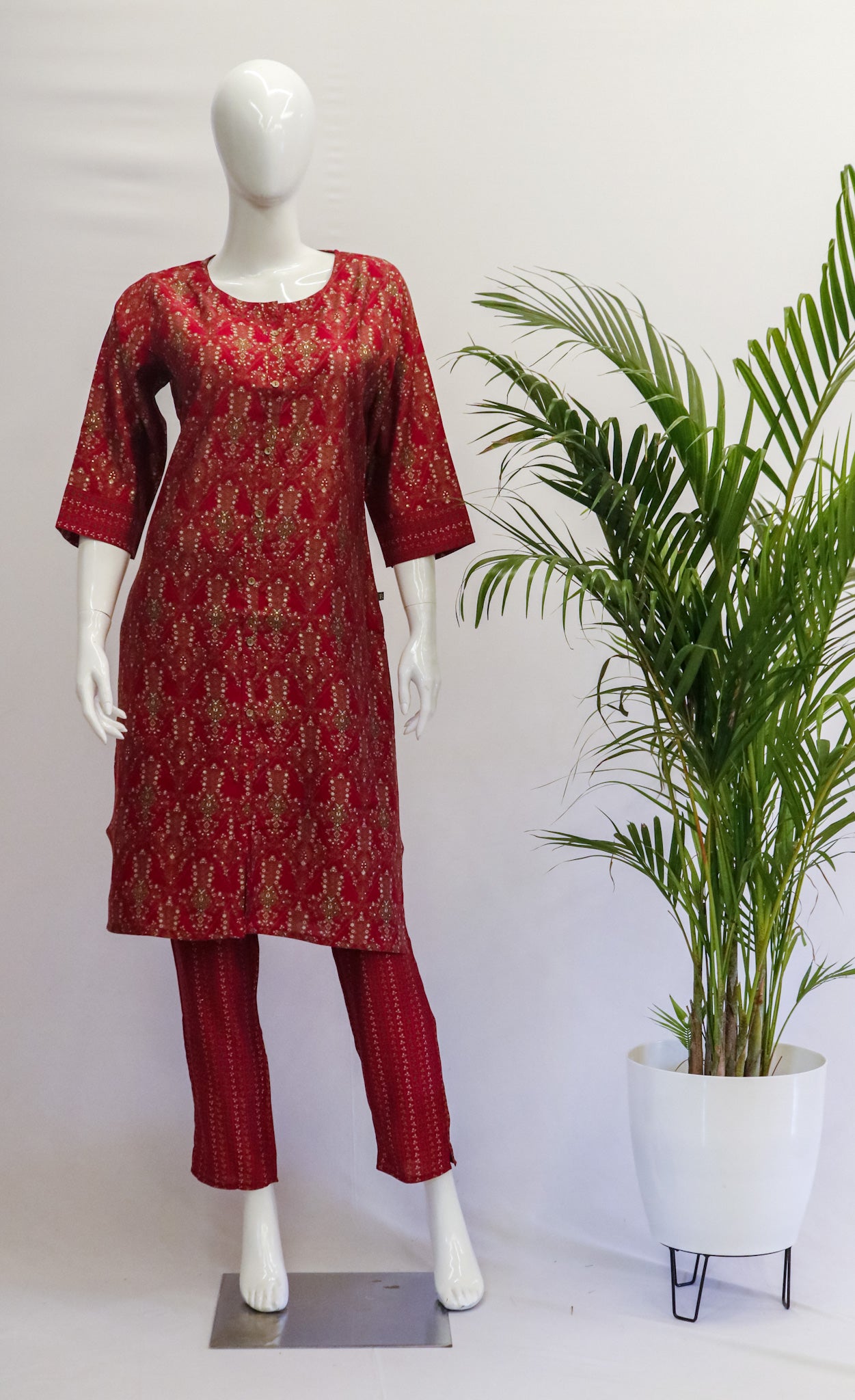 A mannequin displaying a pink muslin top and pant set with floral prints, standing in a retail setting with a tropical plant beside it.