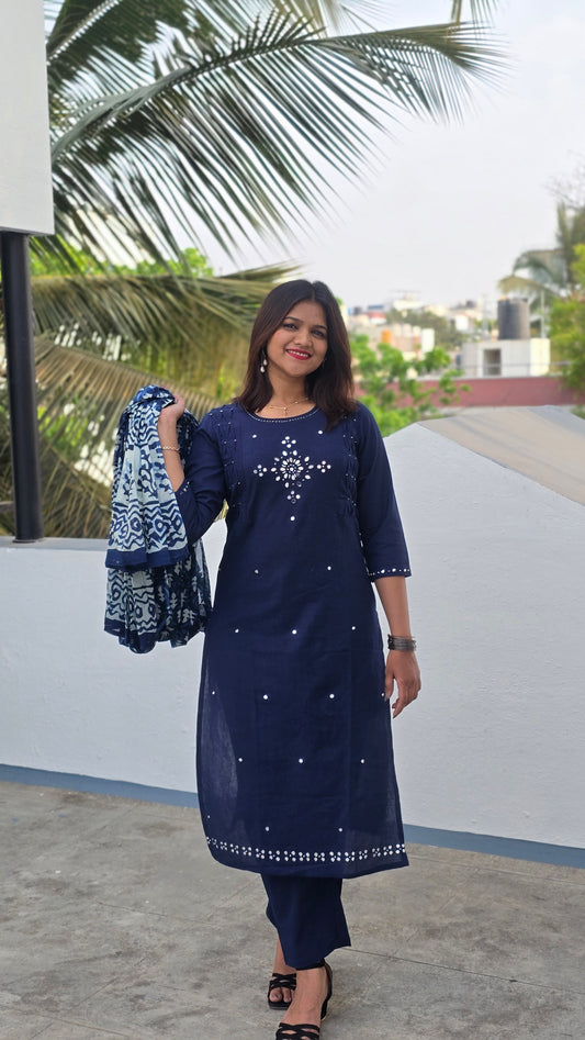 Woman in a blue dress standing outdoors with palm trees in the background