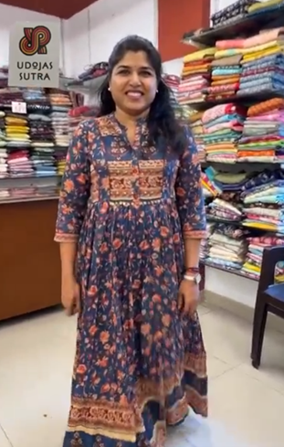 Woman in a patterned dress standing in a fabric store with shelves of colorful fabrics.