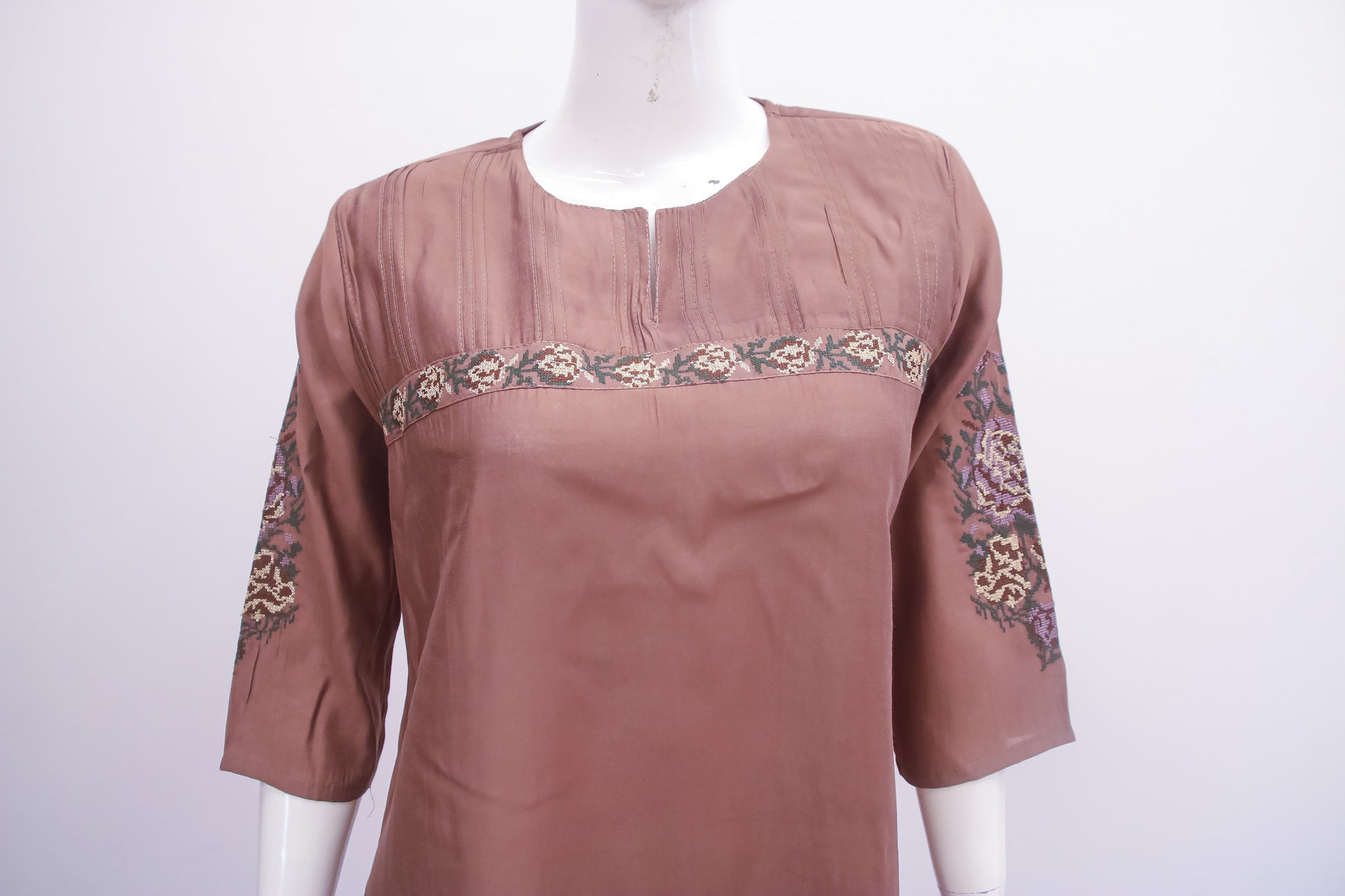 Brown blouse with floral embroidery on a mannequin against a white background