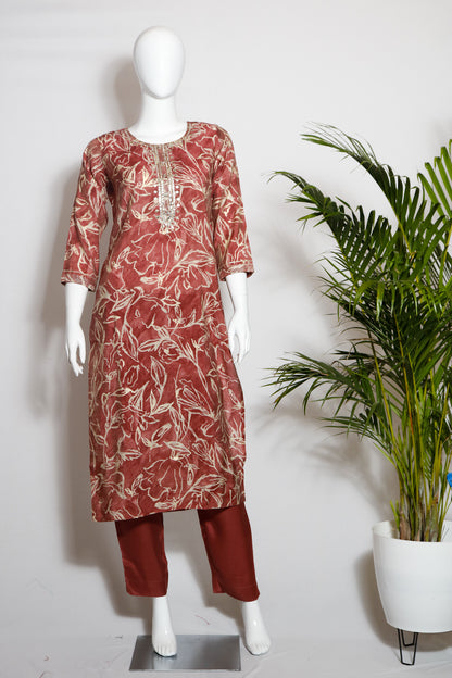A mannequin displaying a muslin silk top and pant set with a floral print, in colors predominantly pink and red, with round neckline and sleeve type visible.