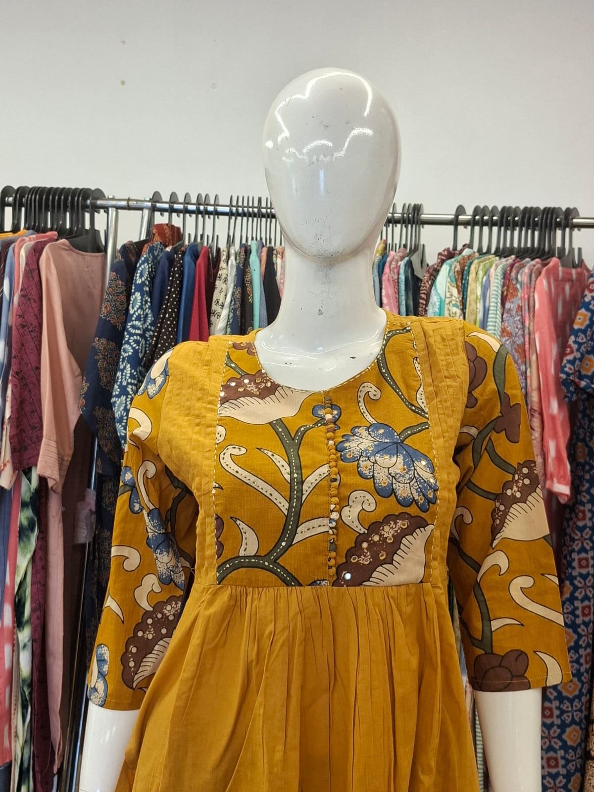 Mannequin wearing a mustard yellow dress with floral patterns in a clothing store.