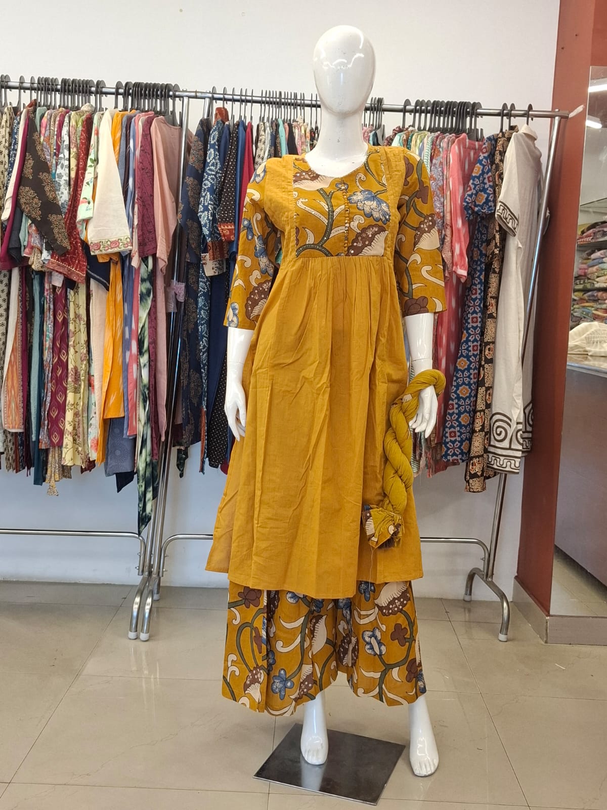 Mannequin wearing a mustard yellow dress with floral patterns in a clothing store.