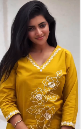 Woman wearing a yellow embroidered dress against a plain background