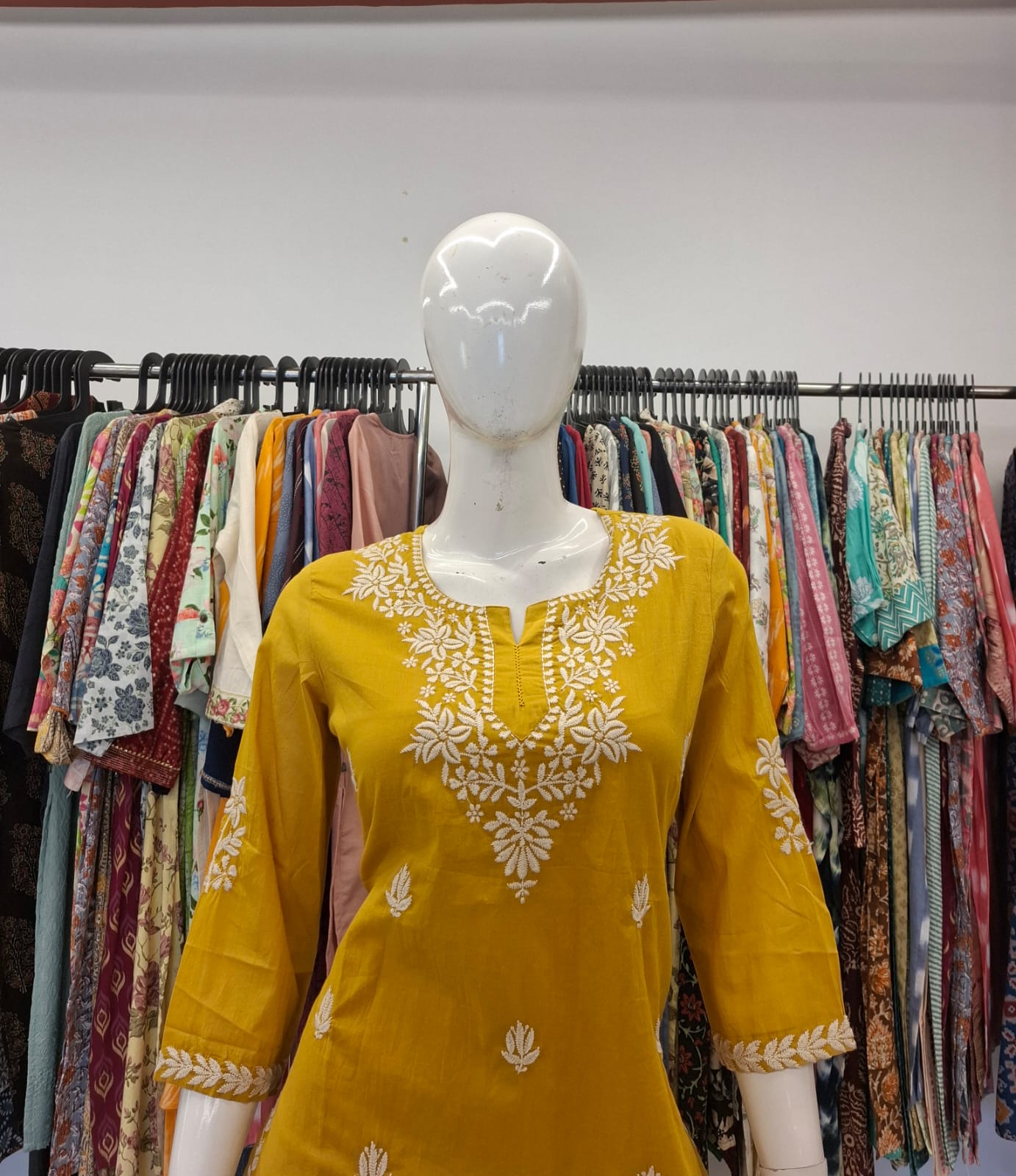 Yellow embroidered dress on a mannequin with a clothing rack in the background