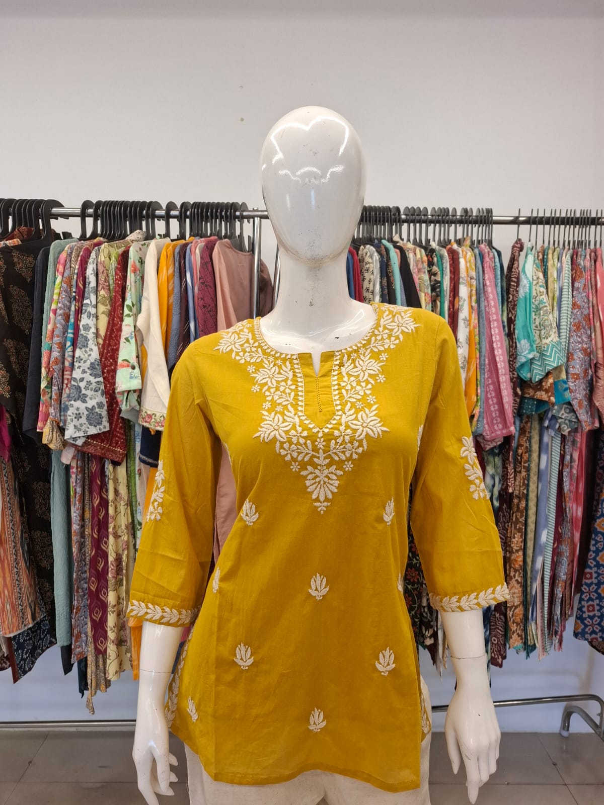 Yellow embroidered top on a mannequin with a clothing rack in the background