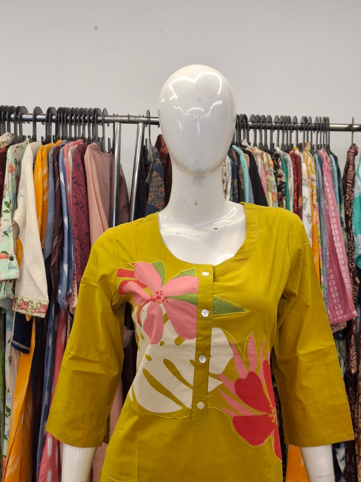 Mannequin wearing a yellow floral shirt with a colorful design in a clothing store.