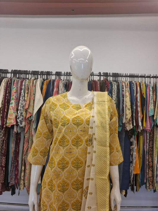 Mannequin wearing a yellow patterned dress with a background of colorful clothes on racks.