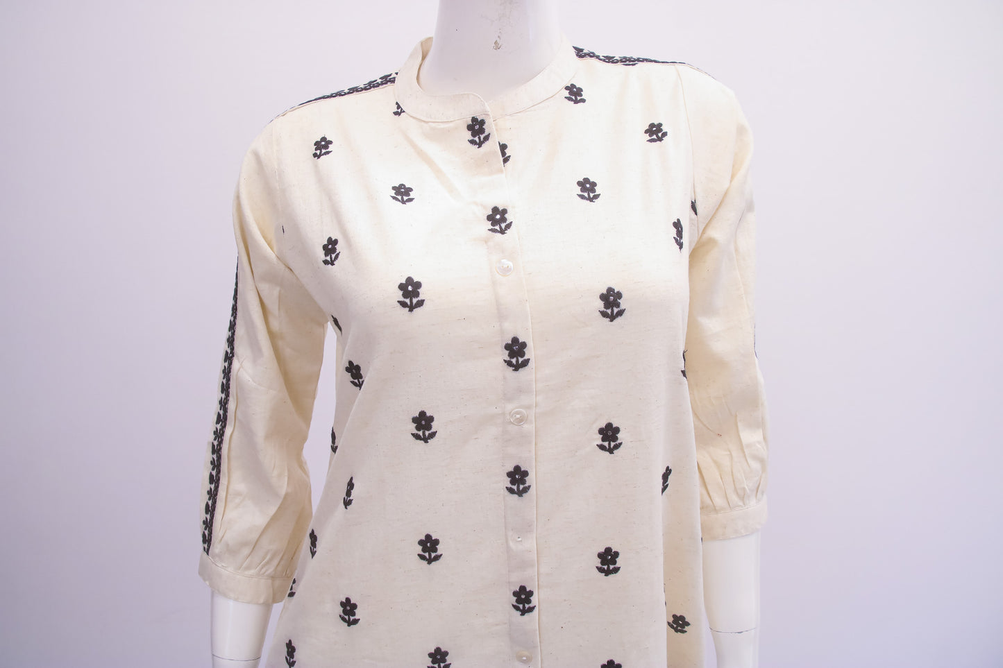 White blouse with black floral patterns on a mannequin against a white background
