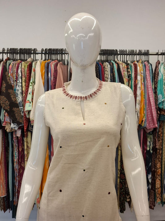 Mannequin wearing a beige dress with a necklace in front of a rack of colorful clothing.