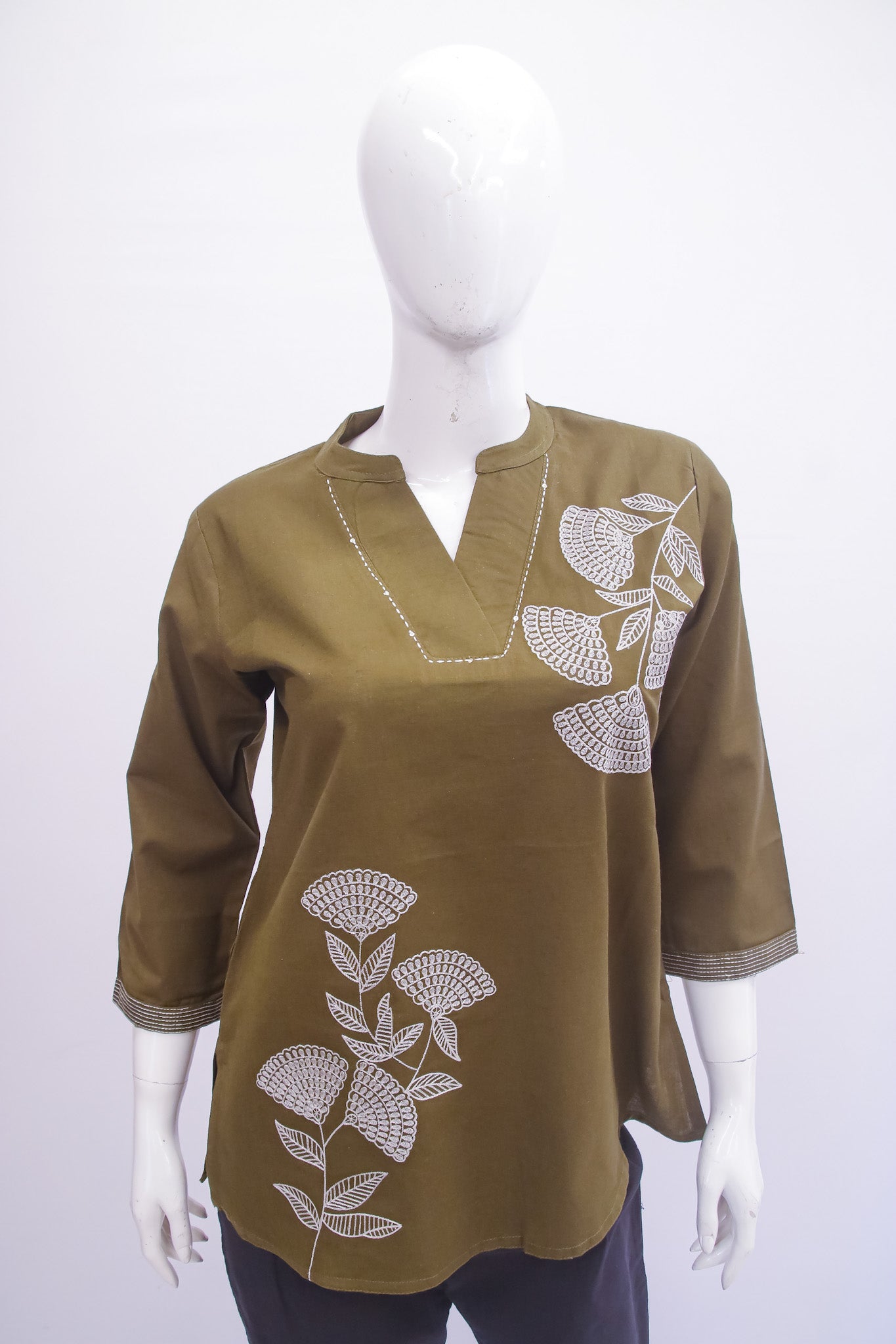 Green blouse with white floral embroidery on a mannequin against a white background