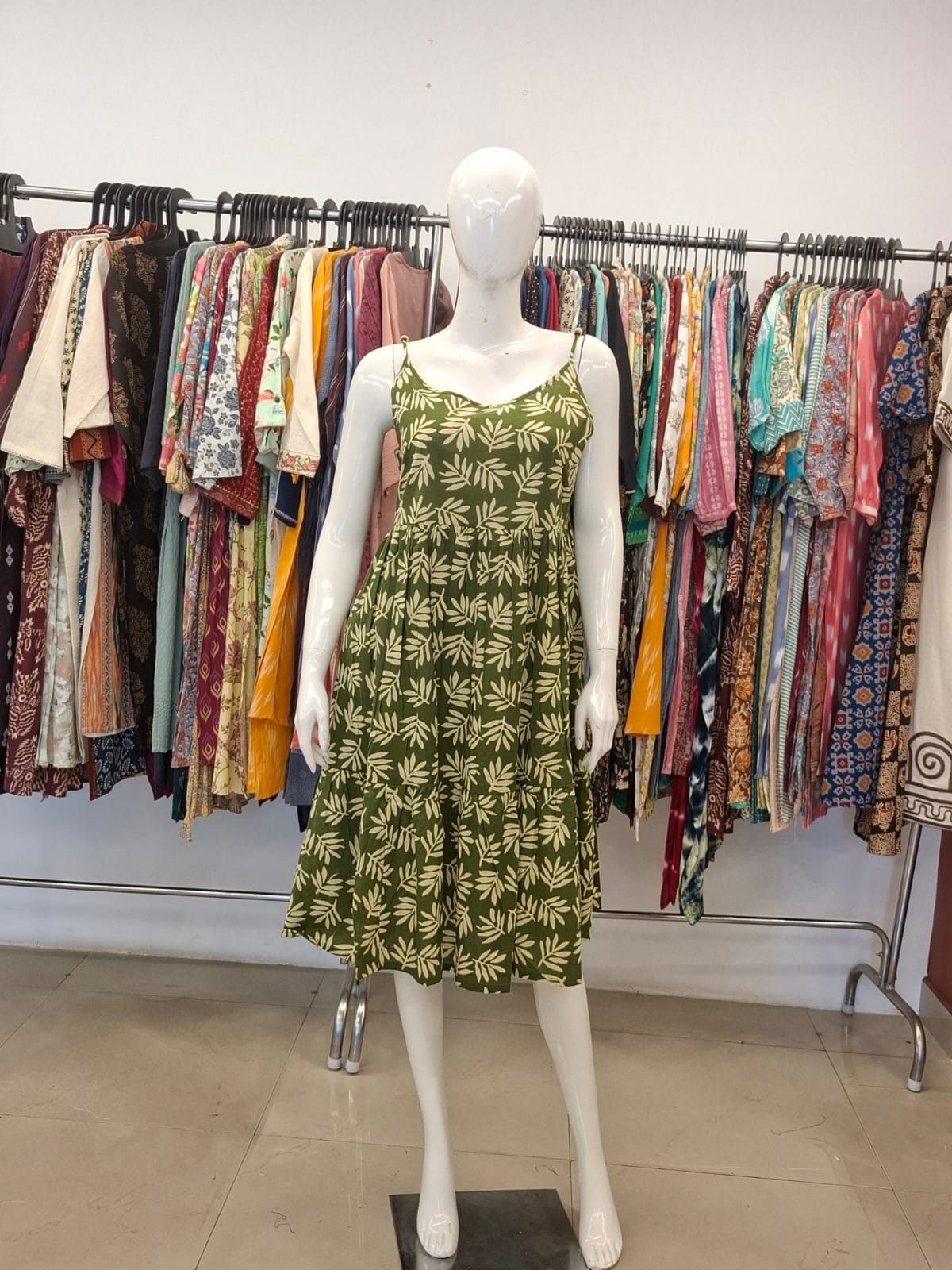 Mannequin wearing a green dress with leaf pattern in a clothing store setting.