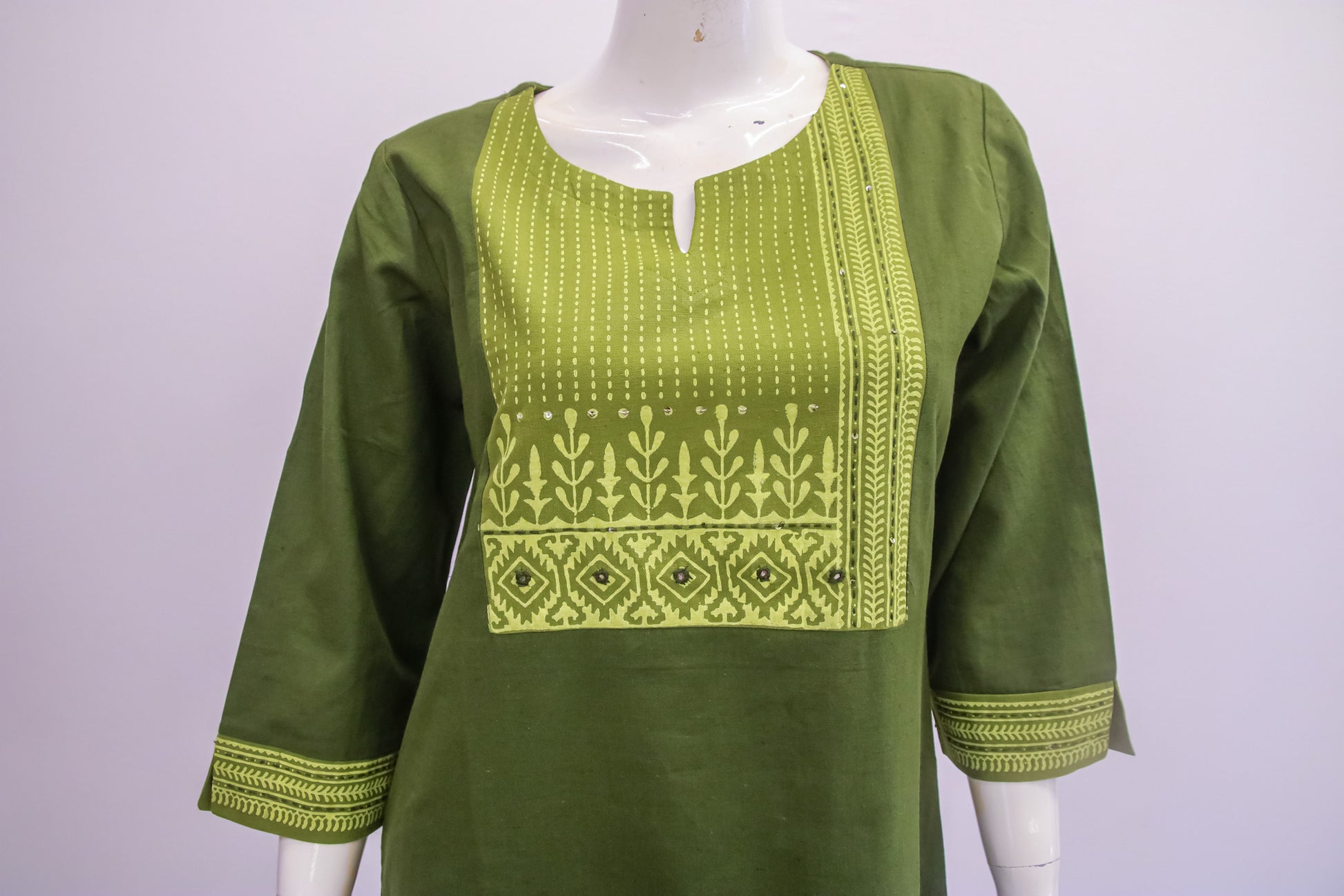 Green embroidered top on a mannequin against a white background