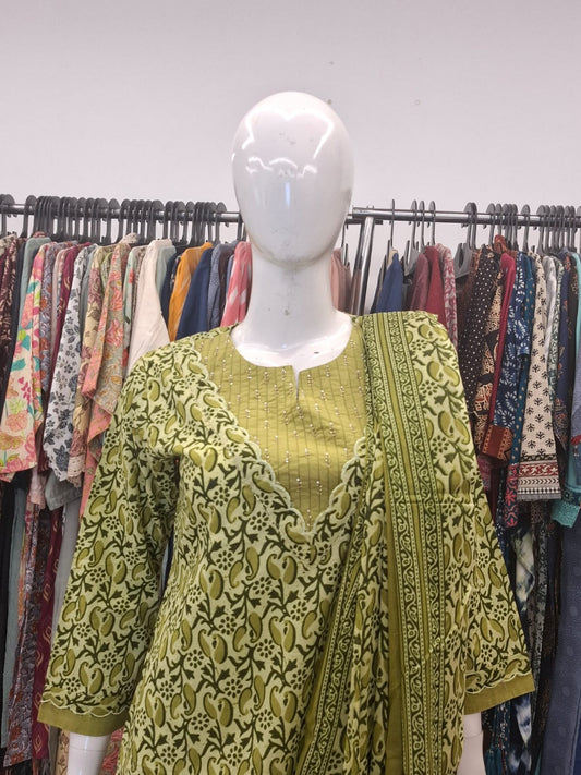 Mannequin wearing a green patterned outfit with a rack of clothes in the background