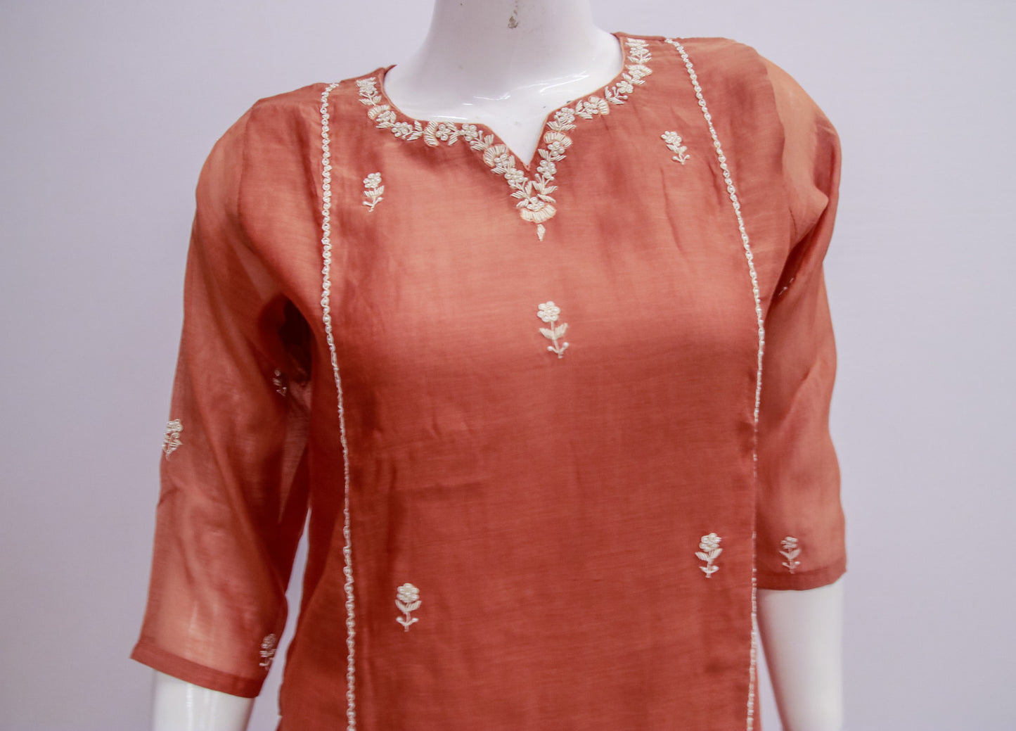 Orange kurta with white embroidery on a mannequin against a gray background