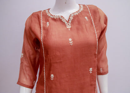 Orange kurta with white embroidery on a mannequin against a gray background