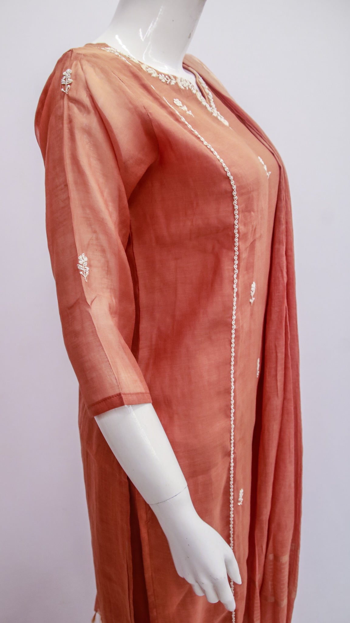 Coral-colored dress with white embroidery on a mannequin against a white background