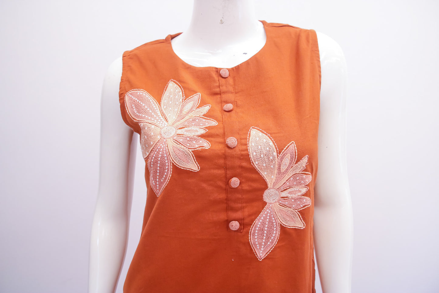 Orange top with floral embellishments on a mannequin against a white background