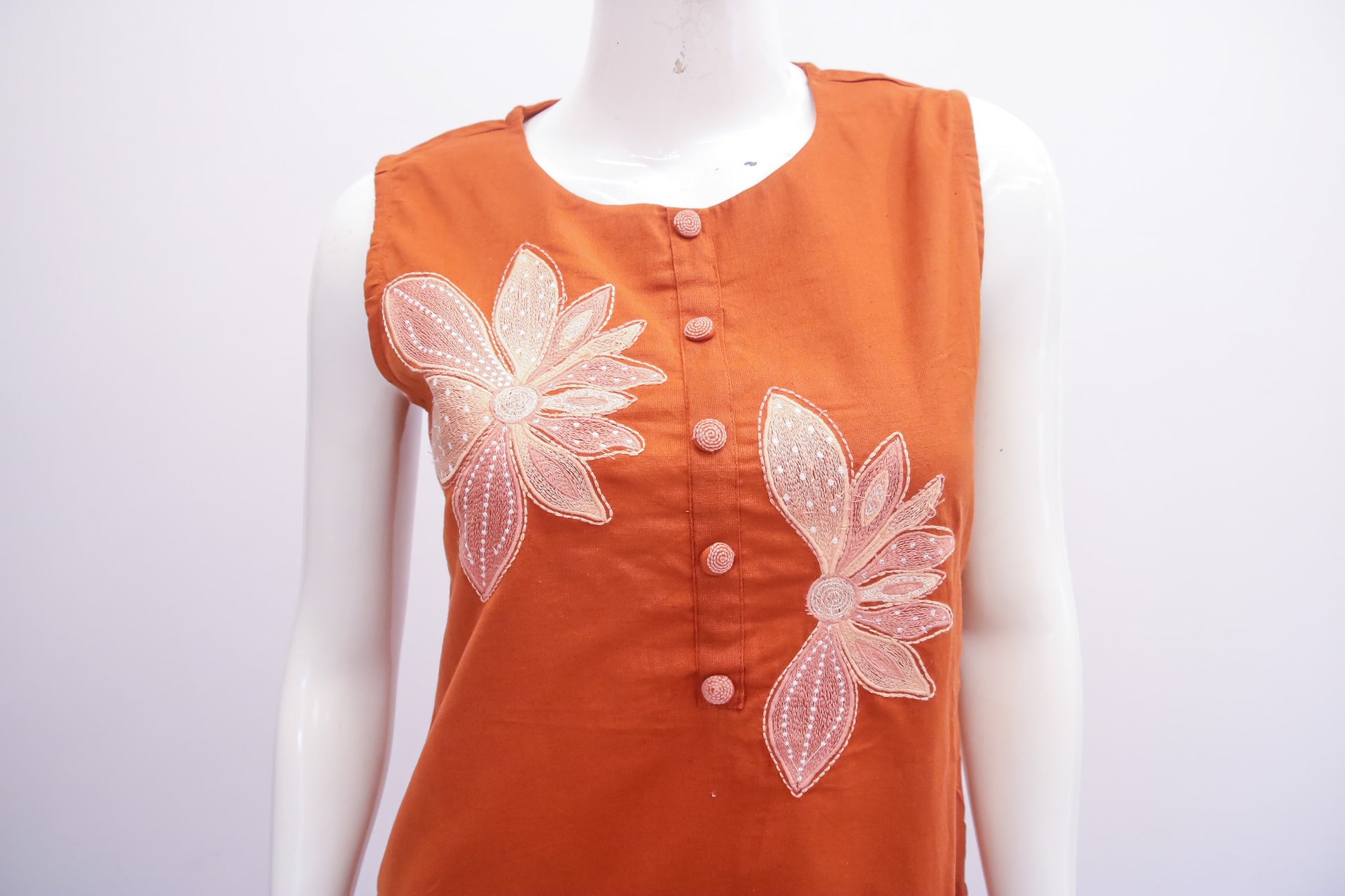 Orange top with floral embellishments on a mannequin against a white background