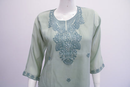 Light green top with blue embroidery on a mannequin against a white background