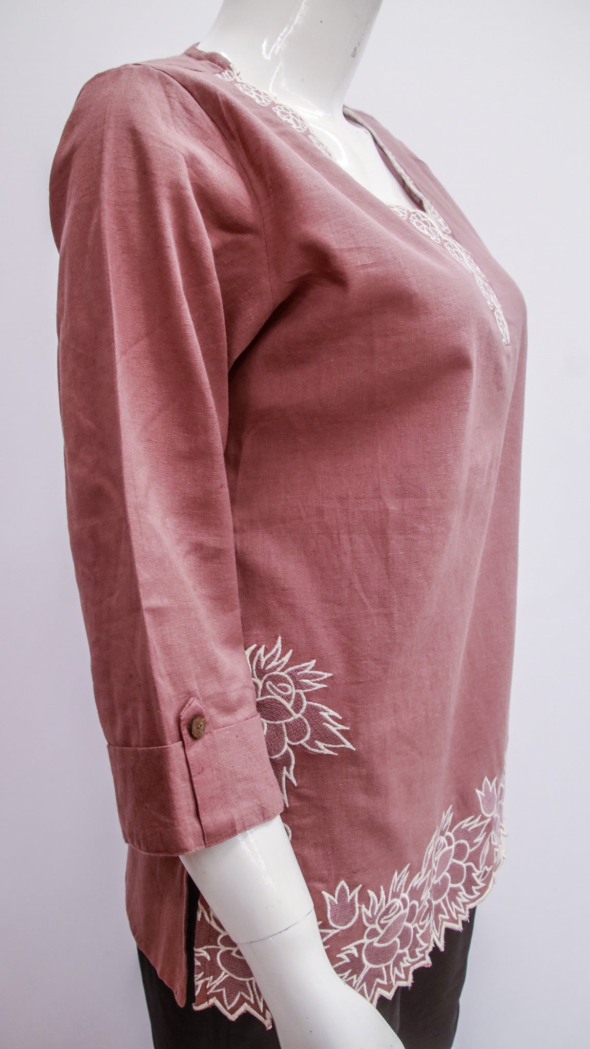 Pink blouse with white floral embroidery on a mannequin against a white background