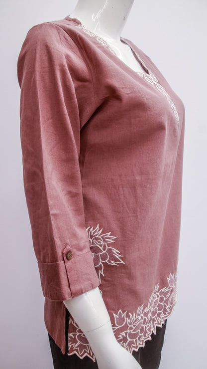 Pink blouse with white floral embroidery on a mannequin against a white background