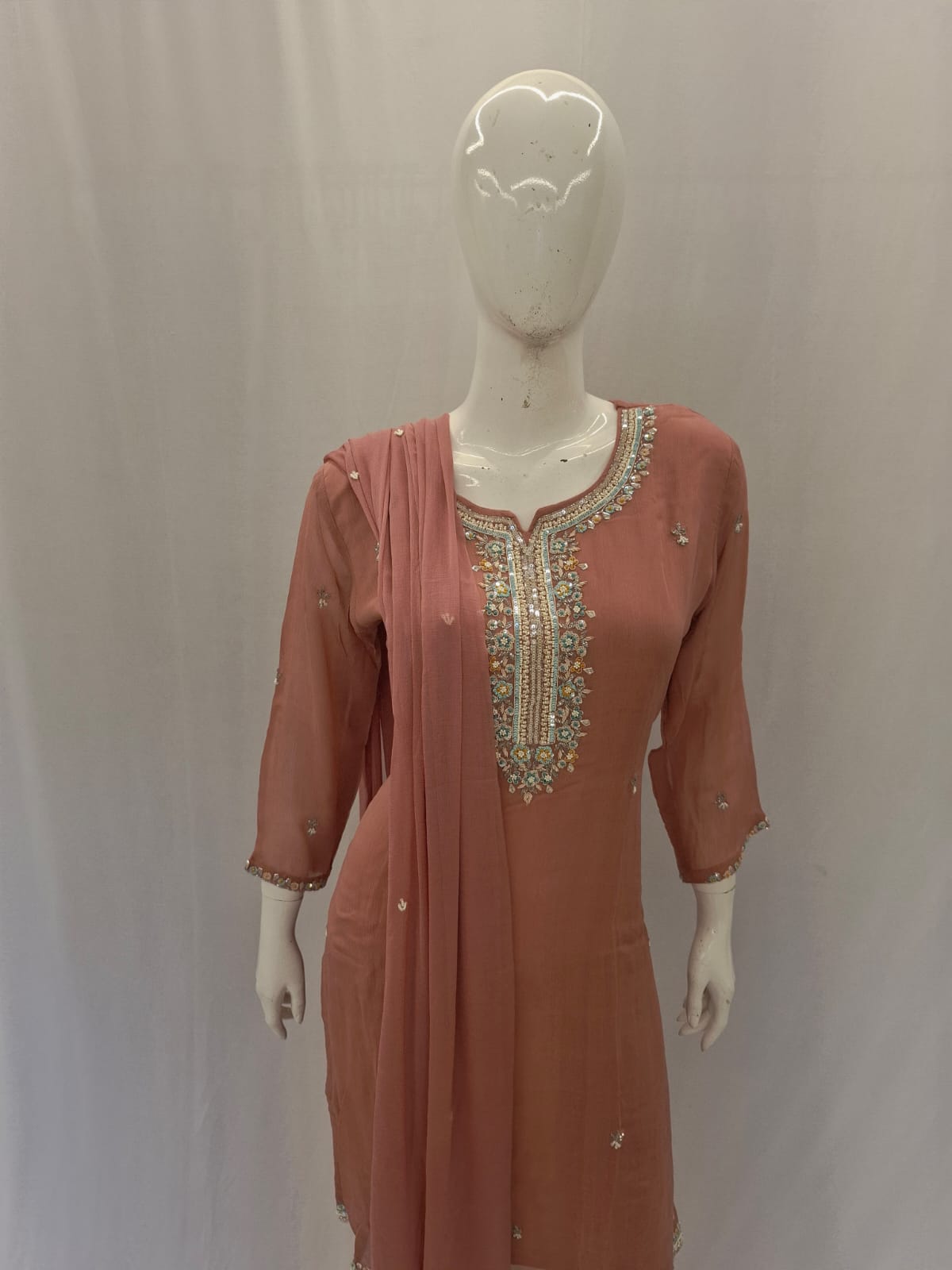 Peach-colored dress with intricate beadwork on a mannequin against a plain background
