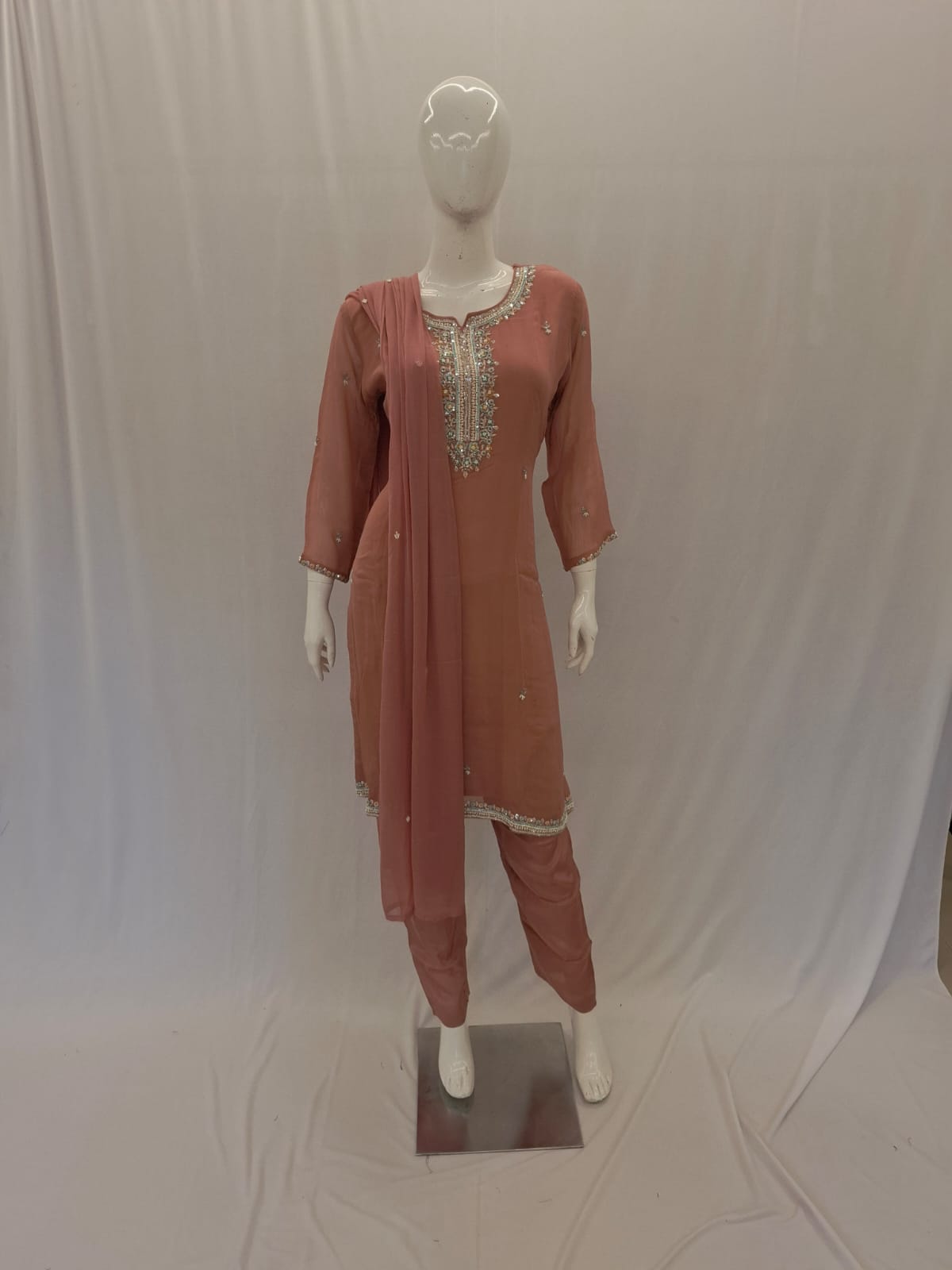Mannequin wearing a rust-colored traditional outfit with intricate embroidery against a plain background