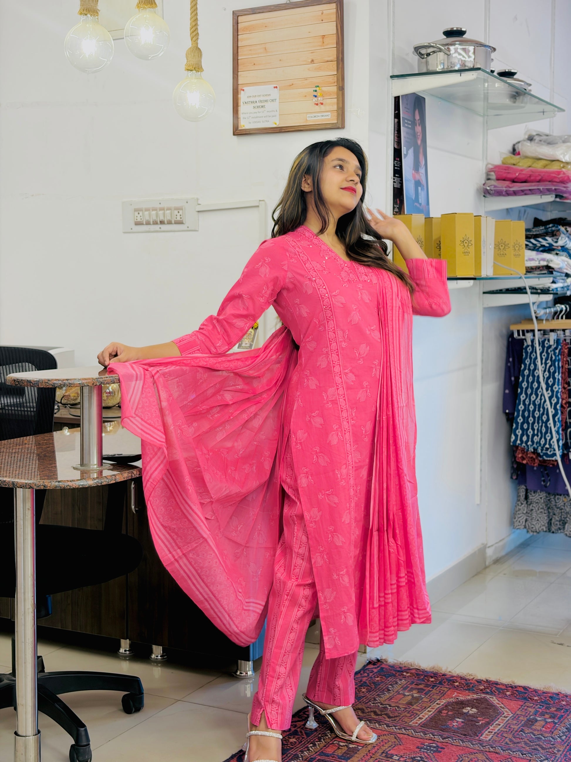 Woman in a pink traditional outfit standing in a room with furniture and decor.