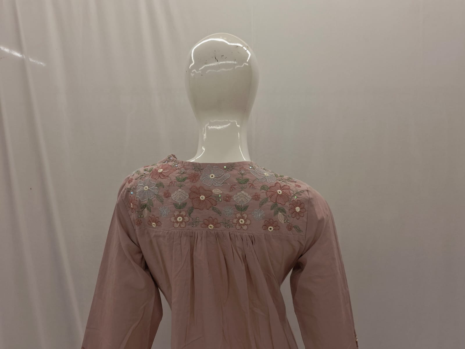 Mannequin wearing a pink blouse with floral embroidery on a plain background