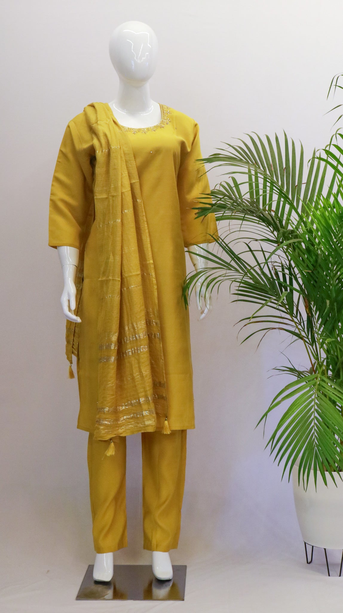 A mannequin displaying a maroon-colored dupatta set with a round neck kurta and straight pants, both made of raw silk, and a cotton silk dupatta with tassels.